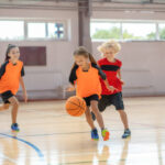 Game. Kids in bright sportswear playing basketball and running after the ball